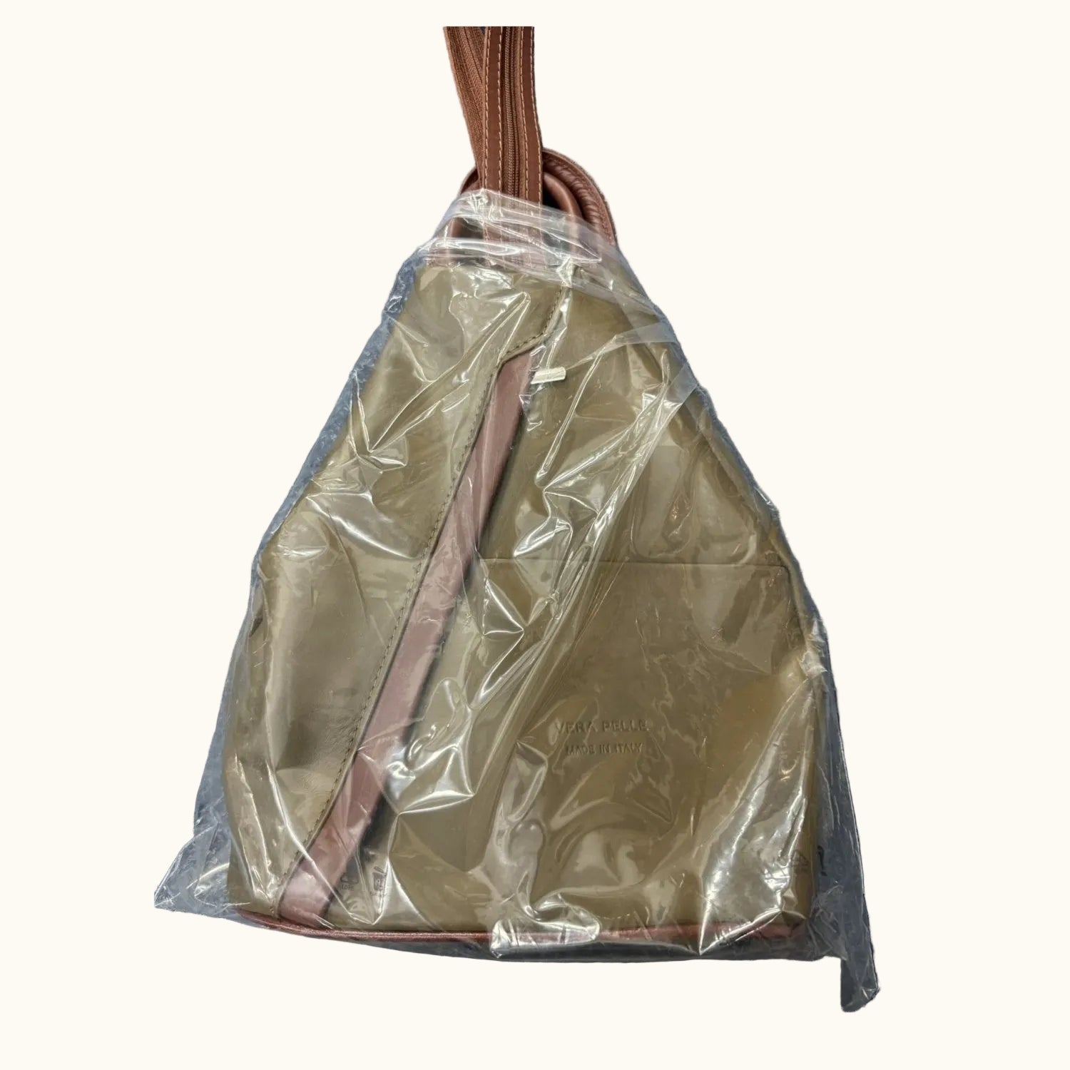 Brown backpack with a brown strap inside clear plastic on a textured gray background