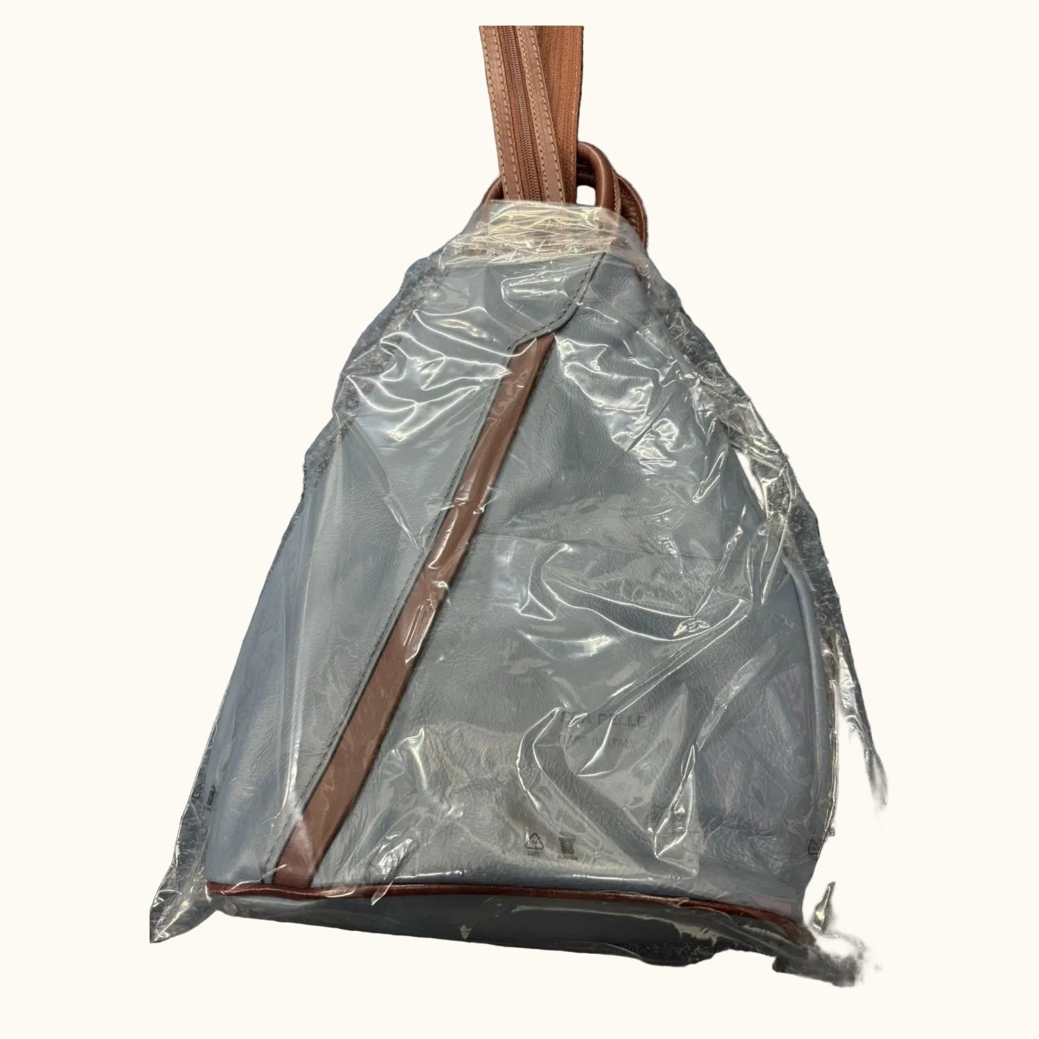Gray backpack with brown straps partially covered by clear plastic on a textured surface